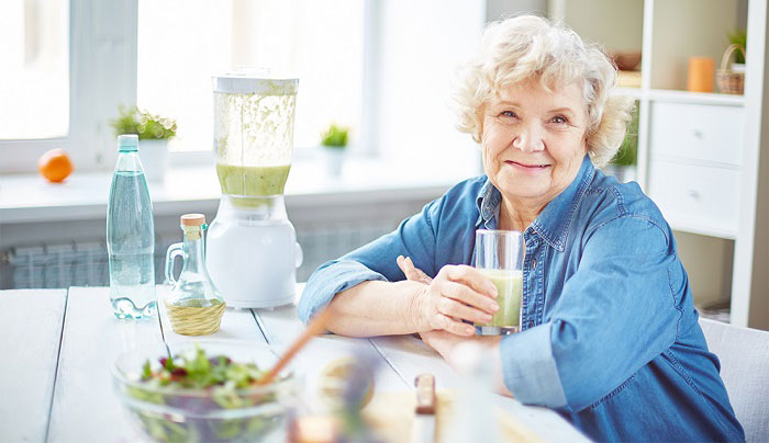 senhora idosa feliz toma suco verde sentada na mesa